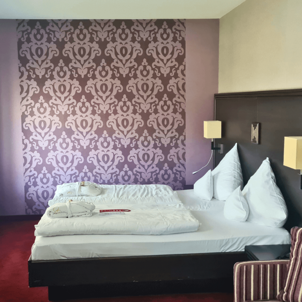 Hotelbett mit lila Tapete im Hintergrund