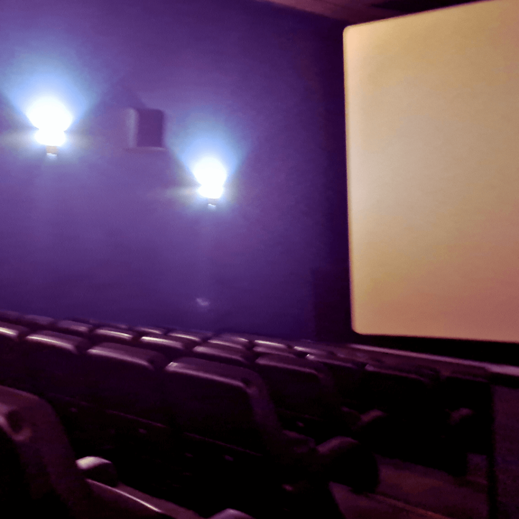Die linke Seit eines Kinosaals, Leinwand, Sitze und Wandbeleuchtung